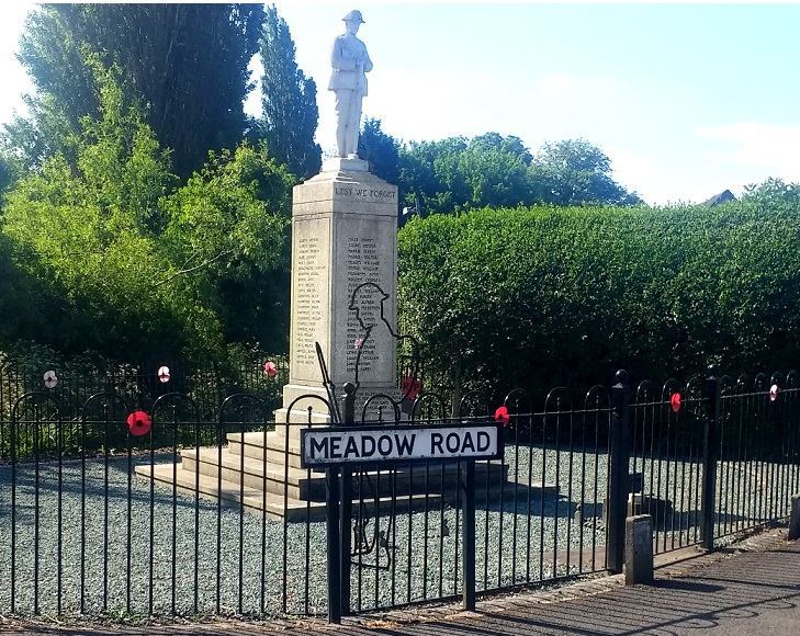 Catshill war memorial on Meadow Road, with a statue of a soldier atop a column bearing names of the fallen. A metal outline of a soldier. In the foreground, the black metal fence is decorated with poppies.