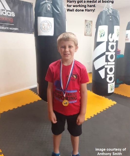 Harry at boxing gym wearing medal he won for hard work. Punchbags in the background.